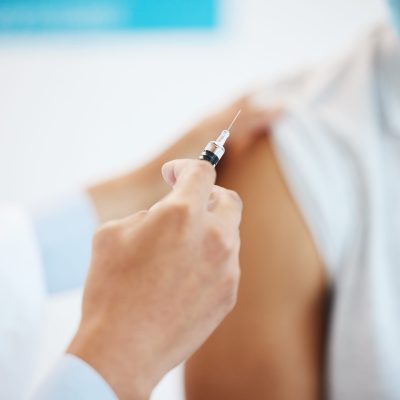 Cropped shot of an unrecognizable doctor injecting her patient with the Covid vaccine in her clinic.